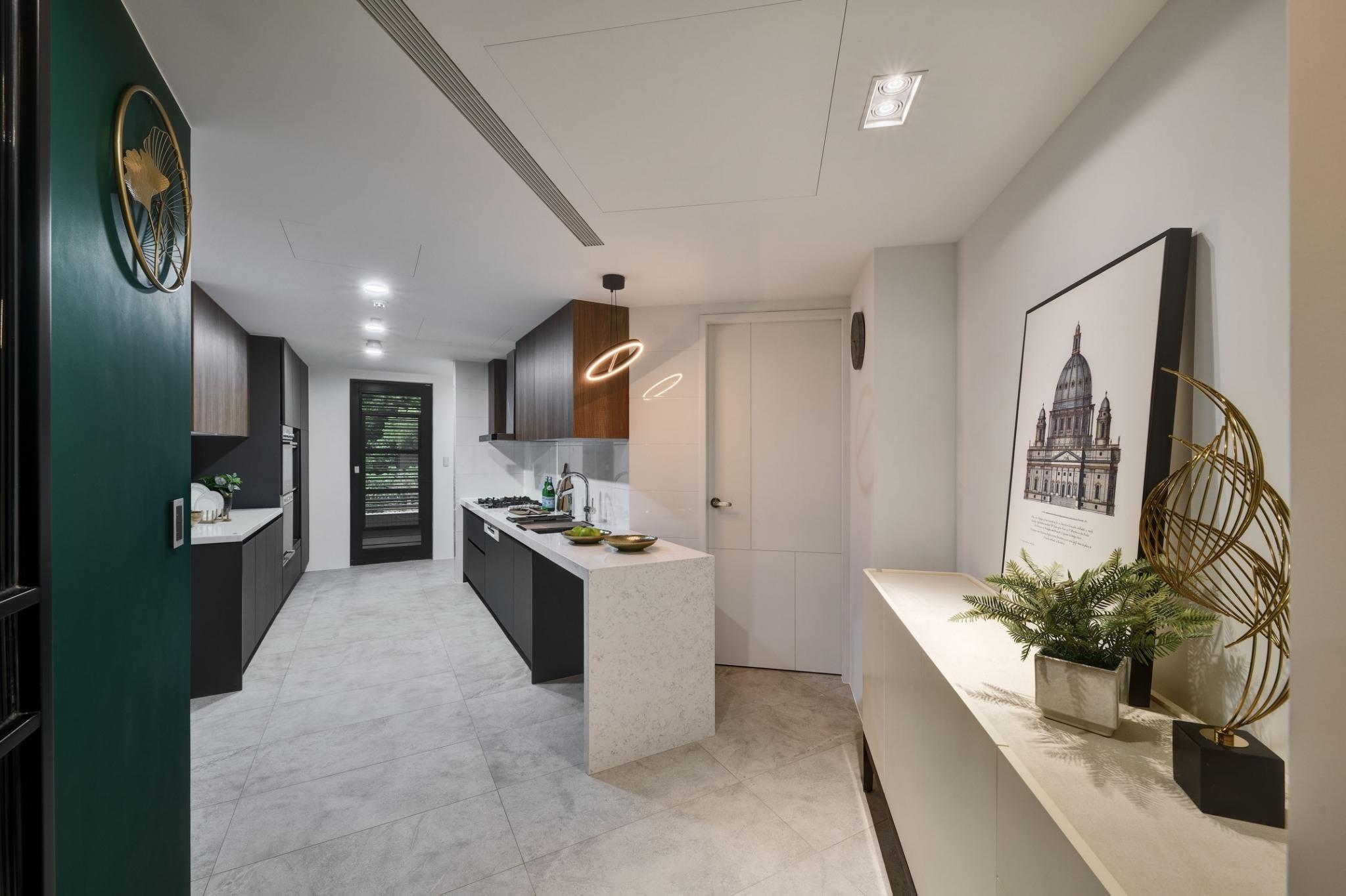 廚房空間亦有一小玄關，石材檯面與黑色櫃體層次分明，凸顯出木質吊櫃與森林系深綠柱體，輕鬆擁有美...