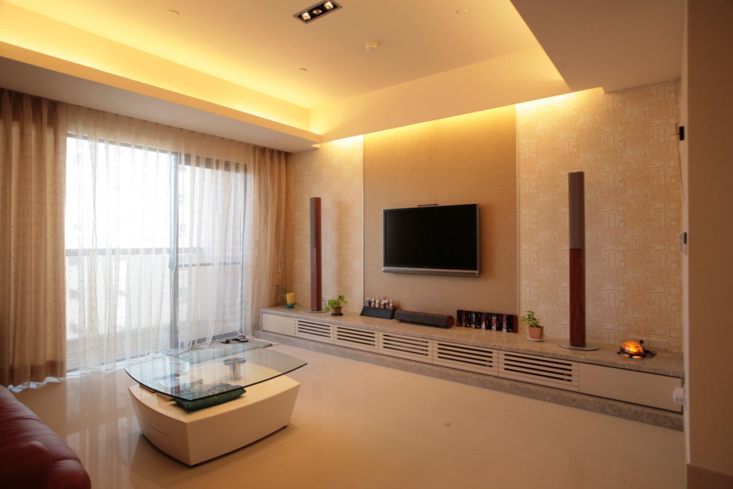 電視牆檯面以延伸的橫向設計強調空間的氣勢，特殊顆粒壁紙的選配以及縱橫交織的燈光設計，在視